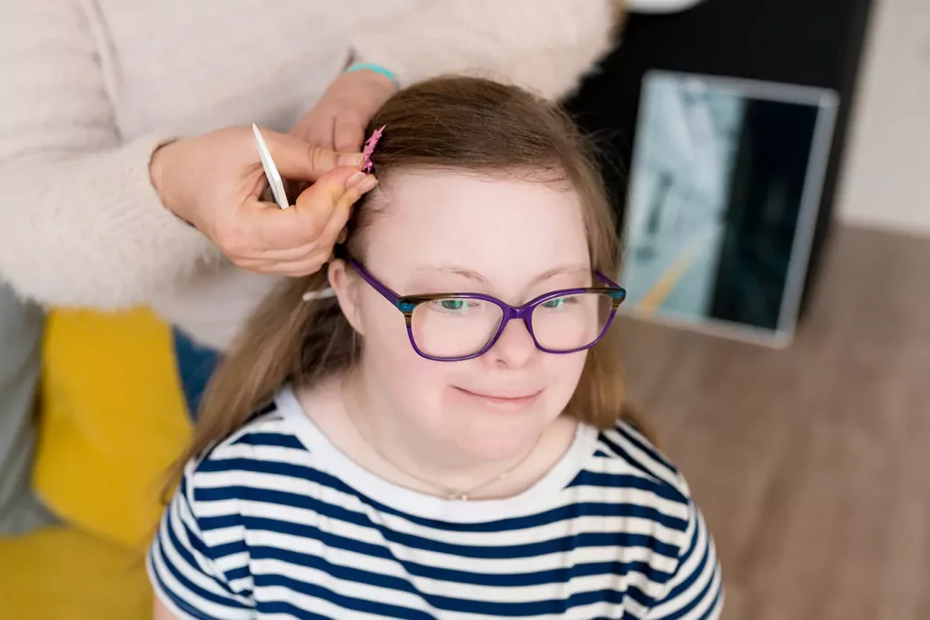 A disabled girl smiling while her support worker does her hair