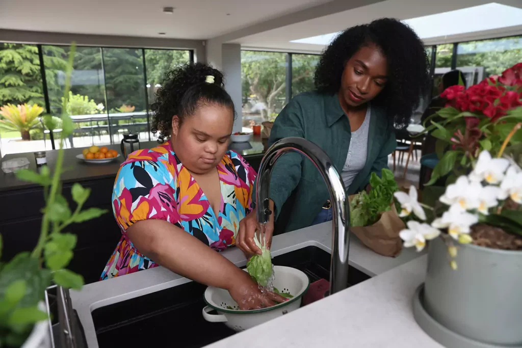 A disabled woman washing vegetables in the kitchen sink with her support worker
